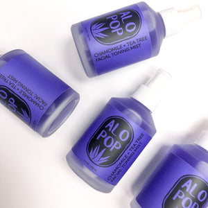 Four glass bottles of Chamomile + Tea Tree Toning Mist. Liquid is purple and the label has the ALOPOP logo and title of this gentle face toning mist in black. The bottles are laying on a white background.
