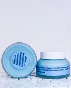 Two blue clarity clay face masks in glass jars with a white screw top lids. One gentle face mask is sitting upright and the other is on it's side to show the bottom round label that has an ingredients list on it. They are Bothe sitting on white geometric tiles with a white background behind it. The acne friendly mask has a blue label with black text.