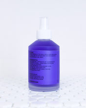 Load image into Gallery viewer, Chamomile + Tea Tree Toning Mist in a glass mist bottle. Liquid is purple and the label has the ingredients list, directions to use and address in black. The bottle is sitting on white tile with a white background.
