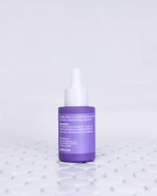 Load image into Gallery viewer, Glass Radiance Facial Oil bottle is sitting on white geometric tiles with a white background. The facial oil is in a muted lavender glass bottle with a matte finish. It has a white dropper top and a lavender label with white text on it. The bottle is facing backwards so that you can see the text that has the usage instructions, natural ingredients list and ALOPOP address/website.